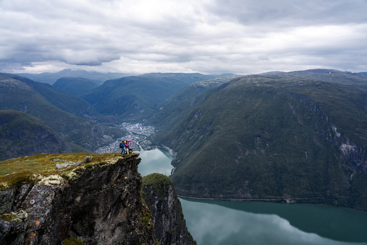 Two hikers and a dog on a cliff high above Øvre Årdal and the fjord